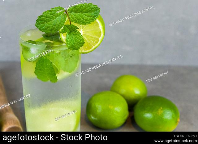 Mojito cocktail glass with mint and lime on a gray concrete background with fresh lime. Sparkling water and refreshing. place for text