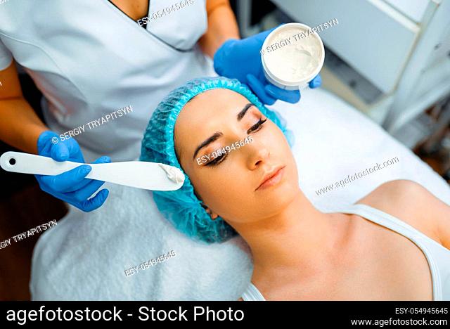 Cosmetician applies the cream to female patient's face, botox preparation. Rejuvenation procedure in beautician salon. Doctor and woman