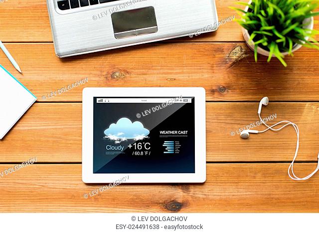 education, business, forecast and technology concept - close up of tablet pc computer, laptop and earphones on wooden table with weather cast