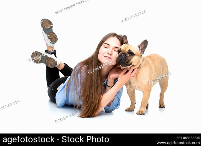 Beautiful young woman with long hair in jeans shirt lying with adult french bulldog girl. Studio shot isolated on white. Copy space