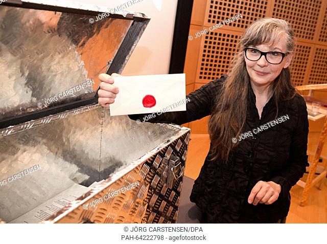 Artist Ulrike Boehme poses with a sealed envelope in front of a box with 100 'secrets' and portraits at the German Historical Museum in Berlin, Germany