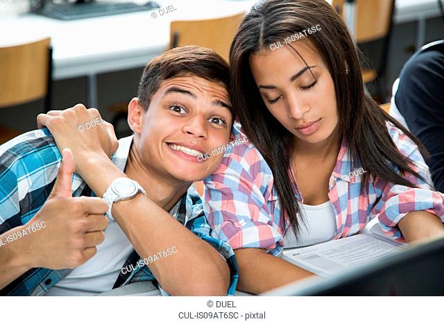 Portrait of teenage boy with cheesy grin and girl with eyes closed in class