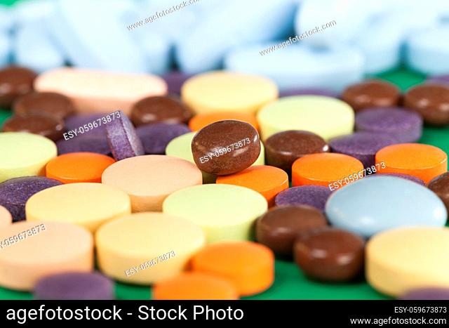 Multi-colored pills on a green background of various packs, a bunch of drugs on paper, medical treatment help, closeup