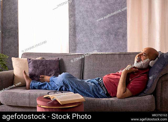 Senior man listening to music with headphone while lying on sofa at home