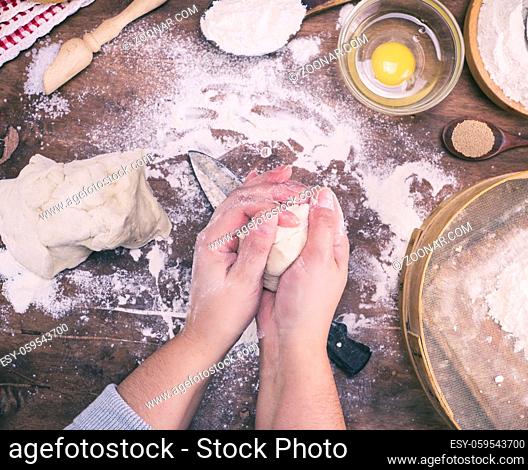 two women's hands mix yeast dough from white wheat flour on the kitchen table, top view