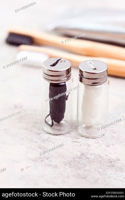 Close up view of two small glass bottles with sustainable dental floss of black and white colors, bamboo toothbrushes on background, blured