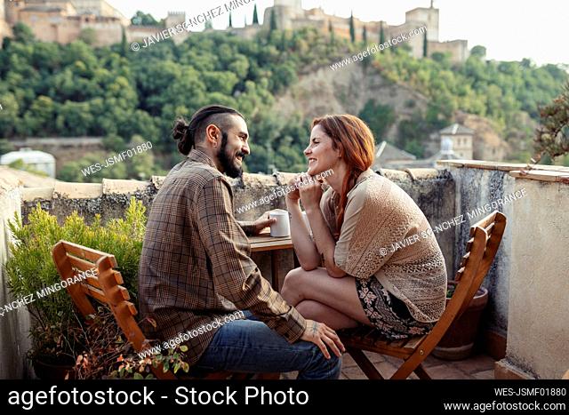 Smiling couple sitting by table on roof top at home