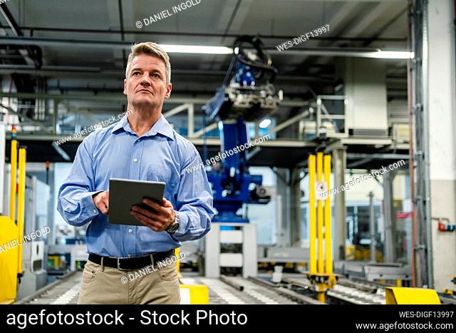 Mature supervisor holding digital tablet while looking away in industry