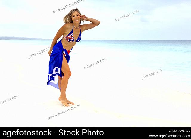 Australian woman beach vibes. Standing on idyllic beach wearing aussie flag sarong and bikini patriotic proud Australian