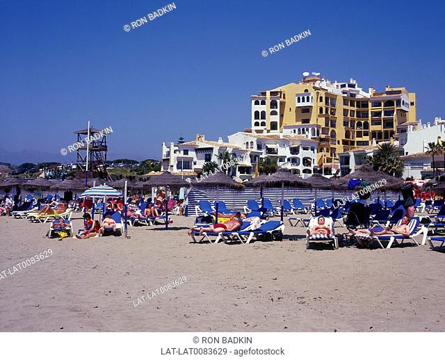 Puerto Cabopino. Houses/ hotels. Sunbeds/ beach umbrellas. People lying in sun