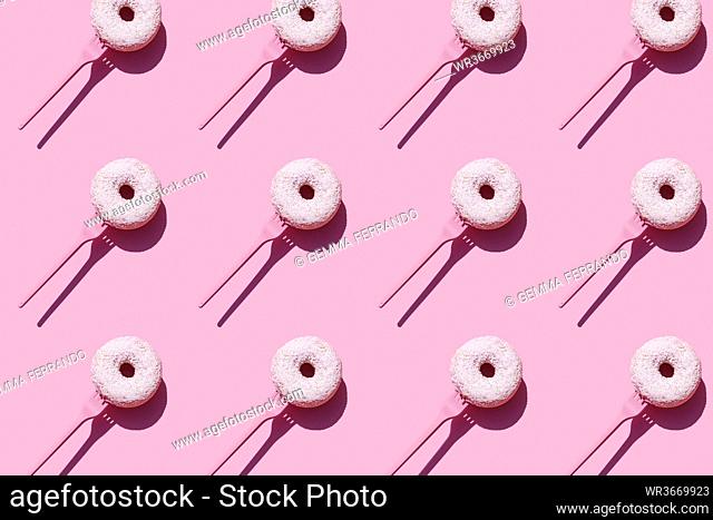 Pattern of forks with sweet doughnuts against pink background