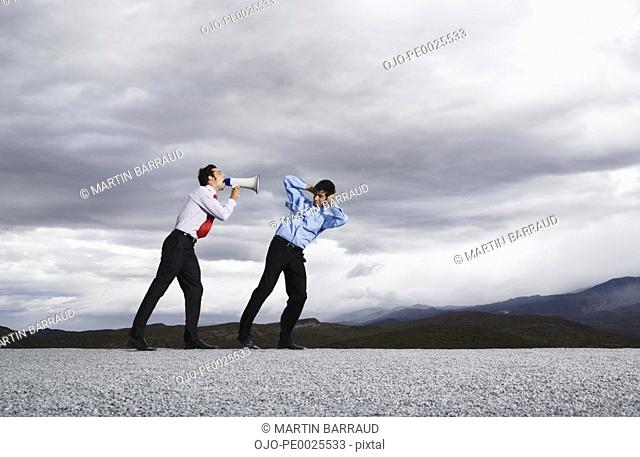 Businessman with megaphone outdoors shouting at man