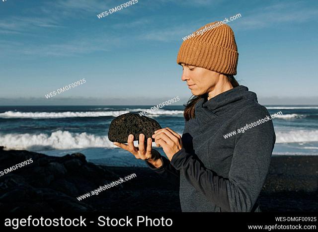 Woman wearing knit hat looking at stone, Janubio Beach, Lanzarote, Canary Islands, Spain