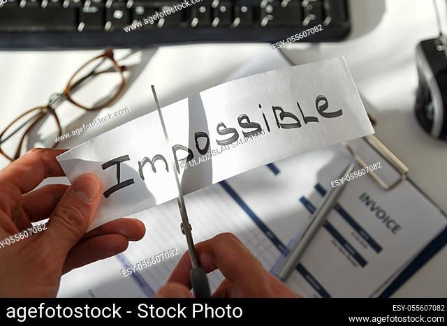Businessman hands cutting the word impossible, letters im so it become possible. Success and motivation concept. Photo at workplace