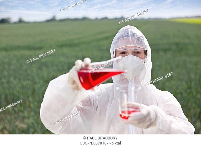 Scientist in protective gear pouring liquid into beaker