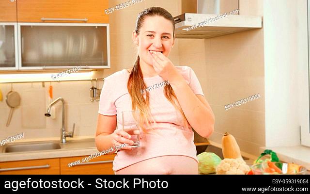 Portrait of smiling pregnant woman taking vitamins in pills and smiling in camera. Concept of healthy lifestyle, nutrition and hydration during pregnancy