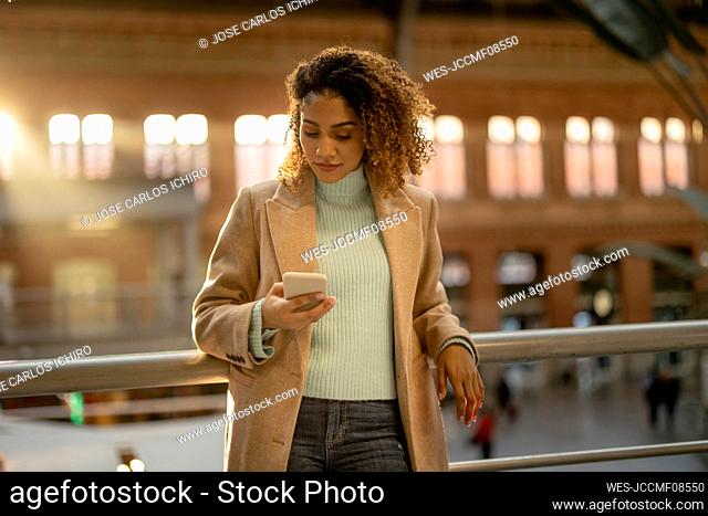 Woman using mobile phone leaning on railing at station