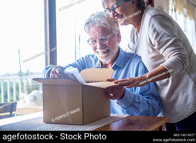 Happy mature aged older family couple unpacking carton box, satisfied with internet store purchase or unexpected gift, feeling excited of fast delivery shipping...