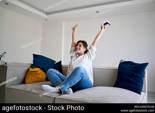 Happy woman with arms raised sitting on sofa at home