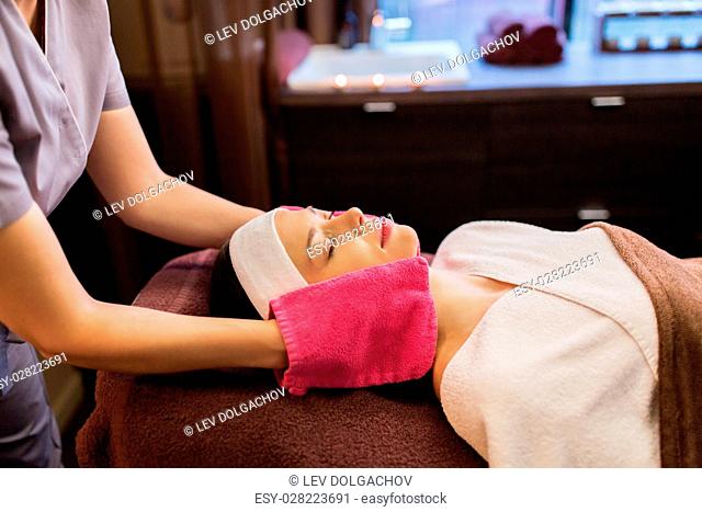 people, beauty, lifestyle and relaxation concept - beautiful young woman lying with closed eyes and having face massage with terry gloves at spa parlor