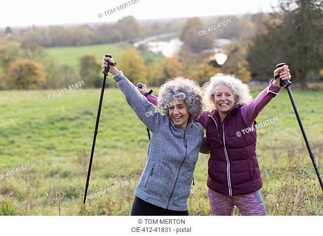 Portrait confident, enthusiastic active senior women friends hiking with poles in rural field