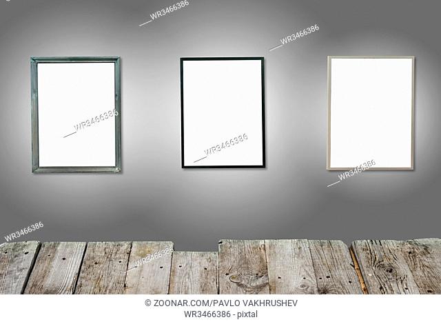 Three white isolated wooden frames on the gray wall with wooden desk