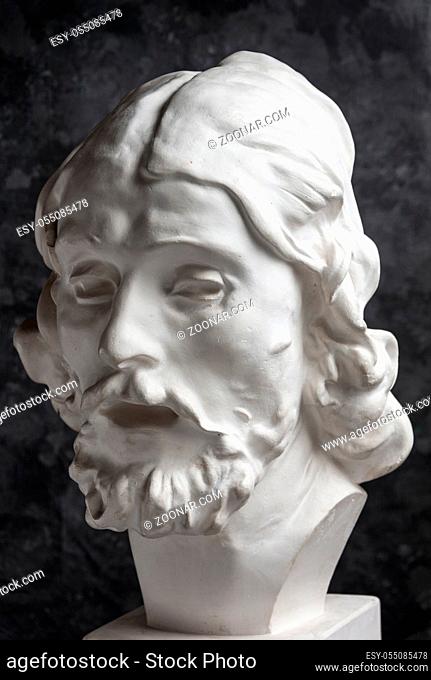 White gypsum copy of ancient statue of John the Baptist head for artists on a dark textured background. Plaster sculpture man face