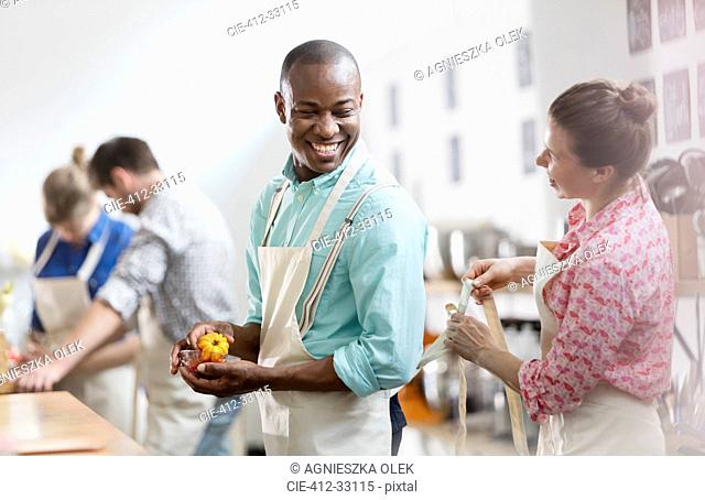 Smiling woman tying apron for man in cooking class kitchen