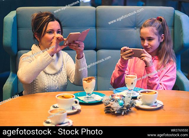 Women taking photos of dessert in coffee shop, using smartphone camera. Candid people, real moments, authentic situations