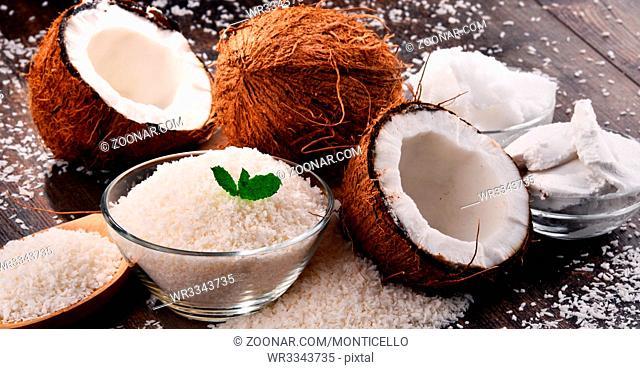 Composition with bowl of shredded coconut and shells on wooden table