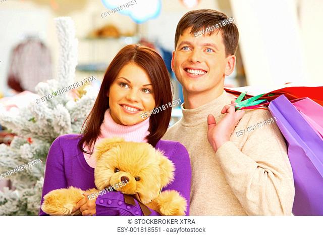 Photo of smiling woman with toy in hands and man holding paperbags in the mall