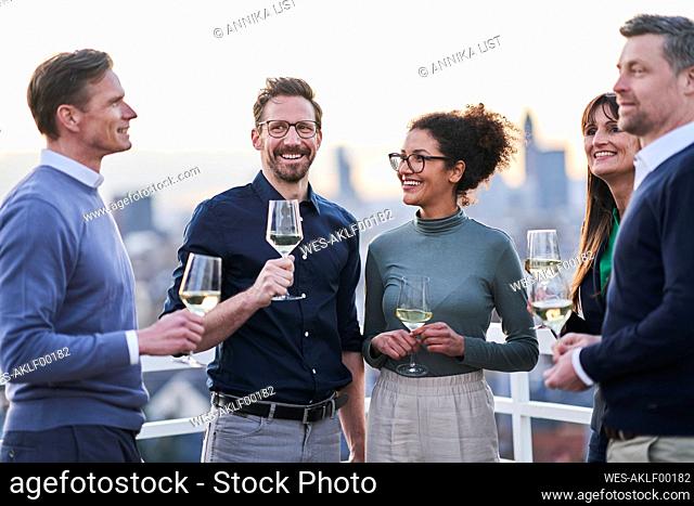Smiling male and female entrepreneurs standing with wineglasses on building terrace