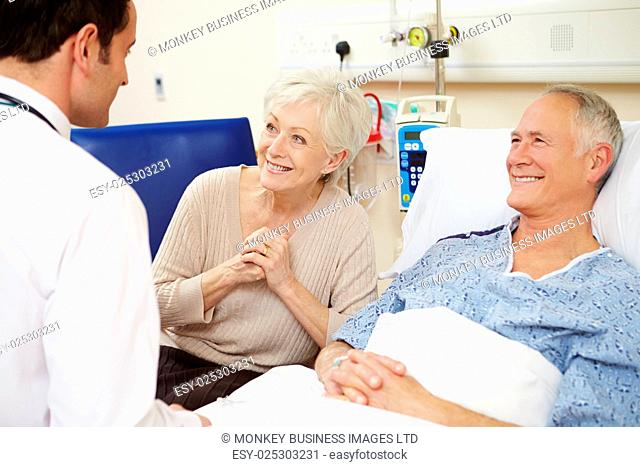 Doctor Talking To Senior Couple By Hospital Bed