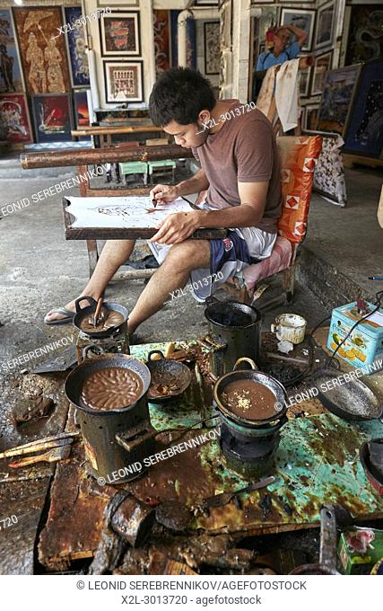 Batik maker applying hot wax-resist dyeing with a canting (spouted tool). Batik Seno shop, Yogyakarta, Java, Indonesia