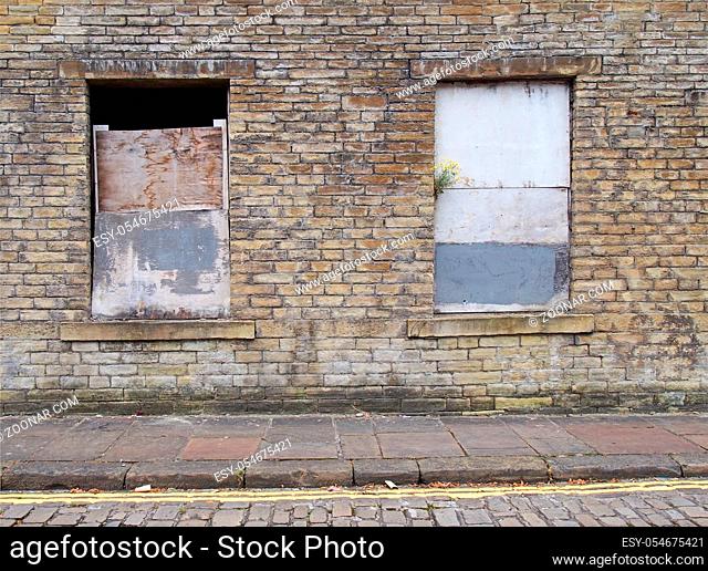front view of an old abandoned derelict house on an empty street with boarded up windows and dilapidated brick walls