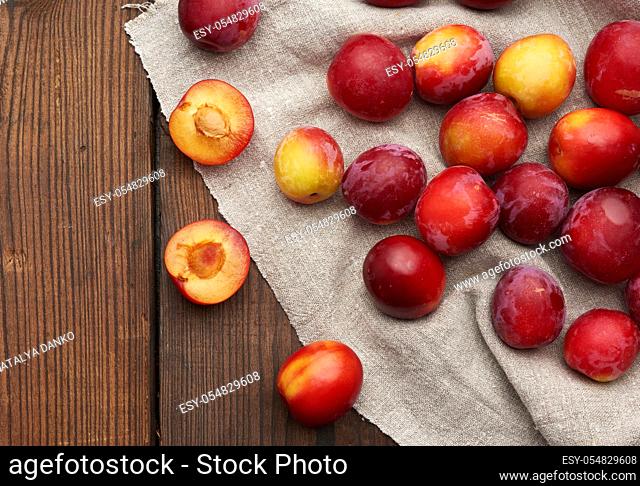 ripe red plums on a gray linen towel, brown wooden table, top view