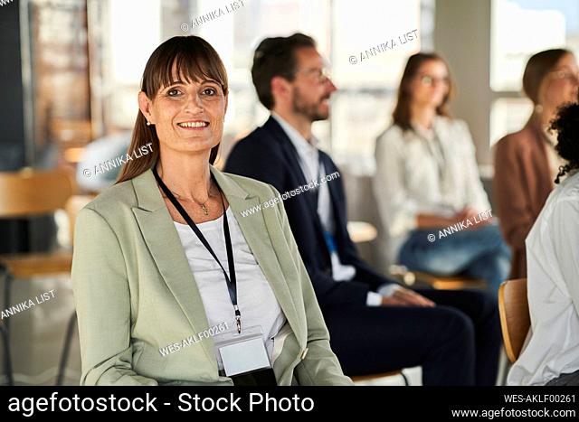 Smiling businesswoman sitting with colleagues at educational event in office