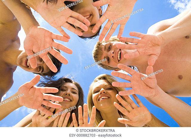 Below angle of several teens keeping their hands in the form of circle with blue sky above