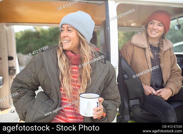 Amigos de las mujeres jóvenes felices bebiendo té en la puerta de la autocaravana