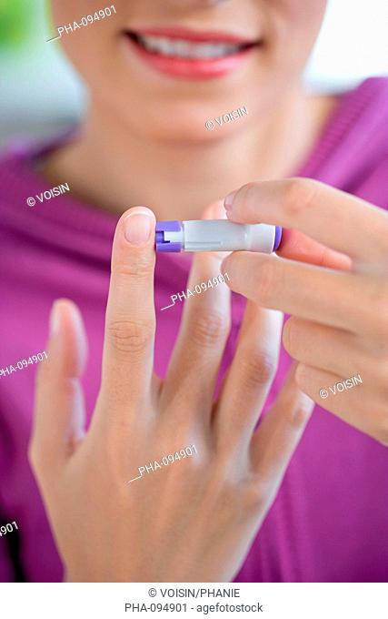 A diabetic person is checking her blood sugar level self glycemia. A drop of blood obtained with a pen-like lancing device here a single-use lancet is placed on...