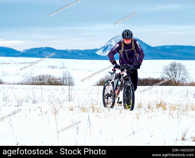 Adult athlete pushes a mountain bike through the snow across a frozen meadow. Hard terrain, the biker can't ride