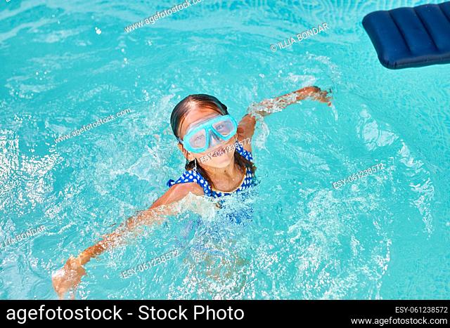 Little girl in goggles having fun, dives and swim in the swimming pool, summer vacation at home, tropical holiday resort