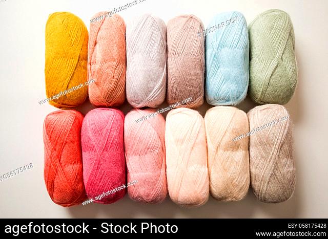 The set of threads for knitting that arranged in two horizontal rows. Threads in pastel colors lie on a white background