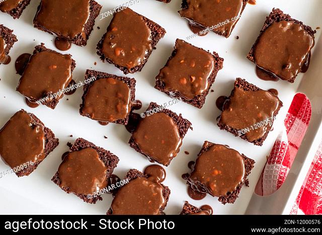 Chocolate brownies covered with chocolate nut ganache - Close up top view of brownie squares in white tray