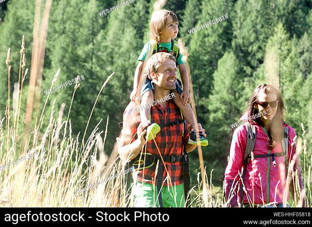 Smiling father carrying son on shoulders while hiking with woman during sunny day