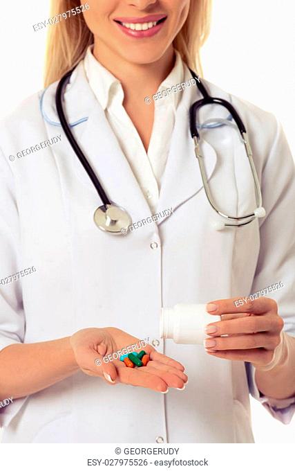 Cropped image of beautiful female doctor in white coat smiling while holding a bottle of medicine and putting pills on her hand, isolated on white background