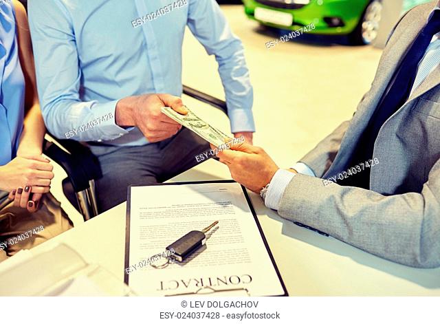 auto business, sale and people concept - close up of customers giving money to dealer and buying car in auto show or salon