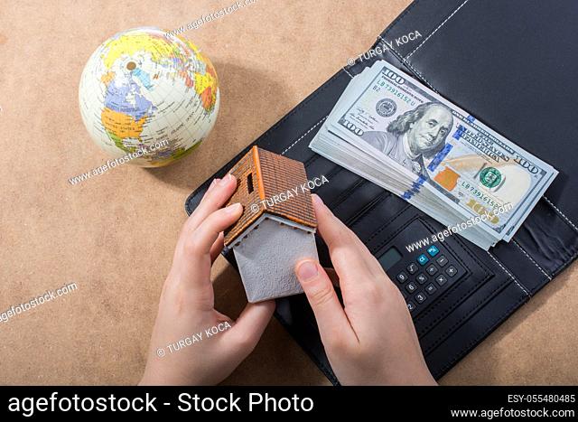 Hand holding house beside American dollar banknotes and globe