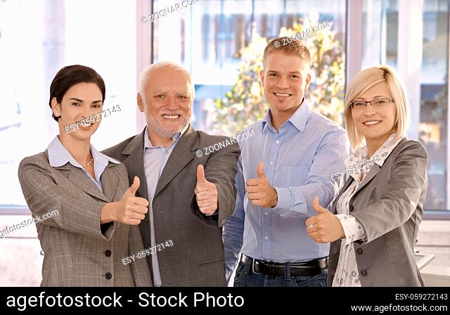 Successful businessteam giving thumbs up standing in bright office, smiling