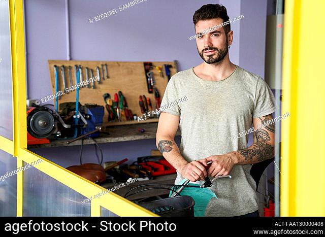 Mid-shot portrait of bearded man standing in his workshop in front of his tools